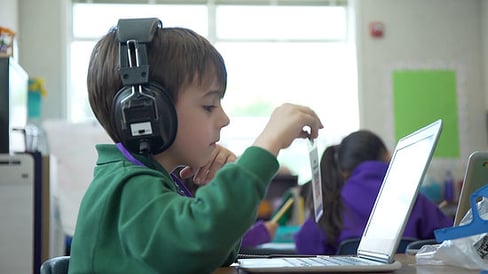 Boy student sitting at desk with laptop open and headphones on for some independent learning